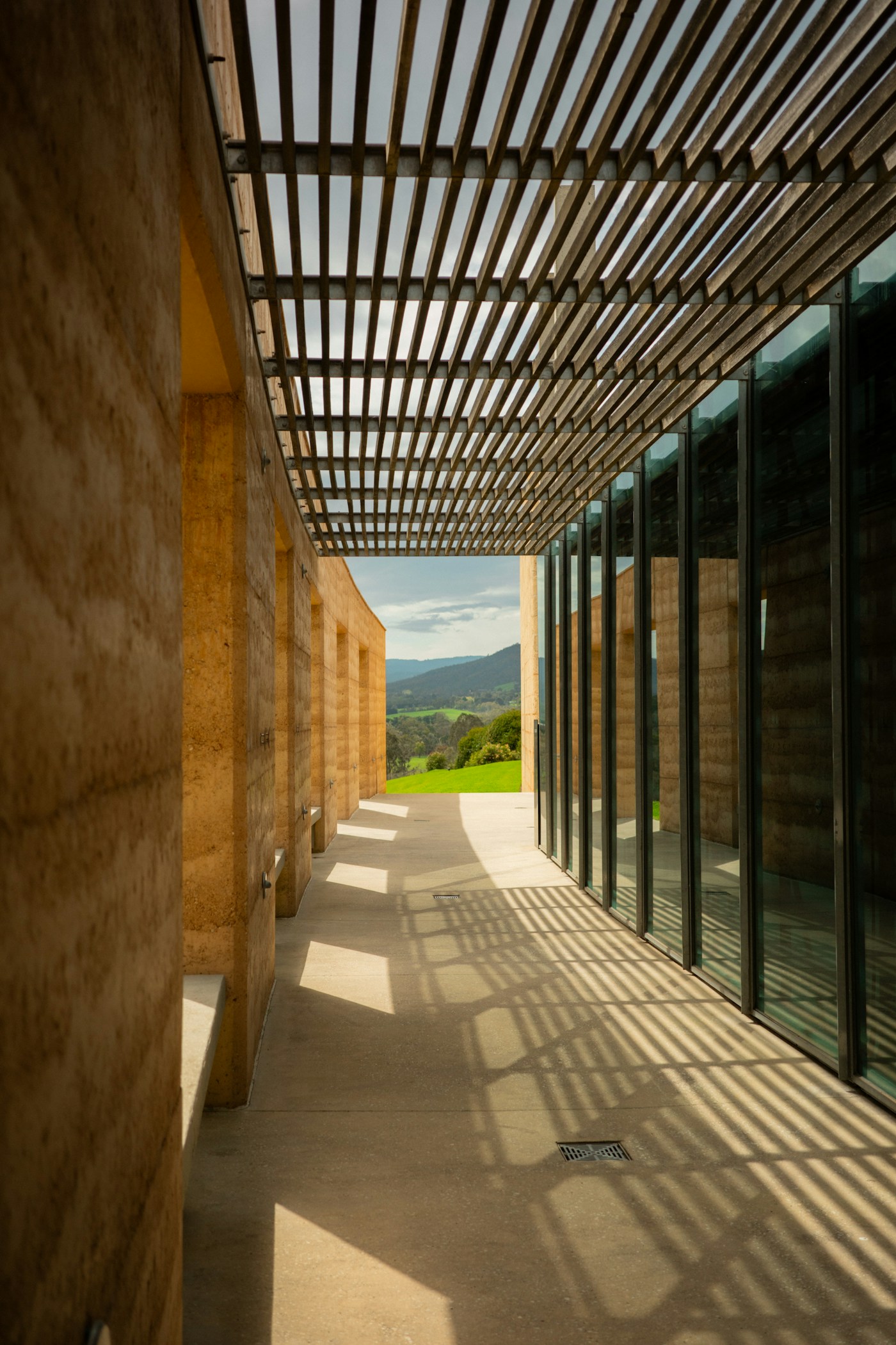 Modern shaded walkway built with natural earth walls and a wooden pergola