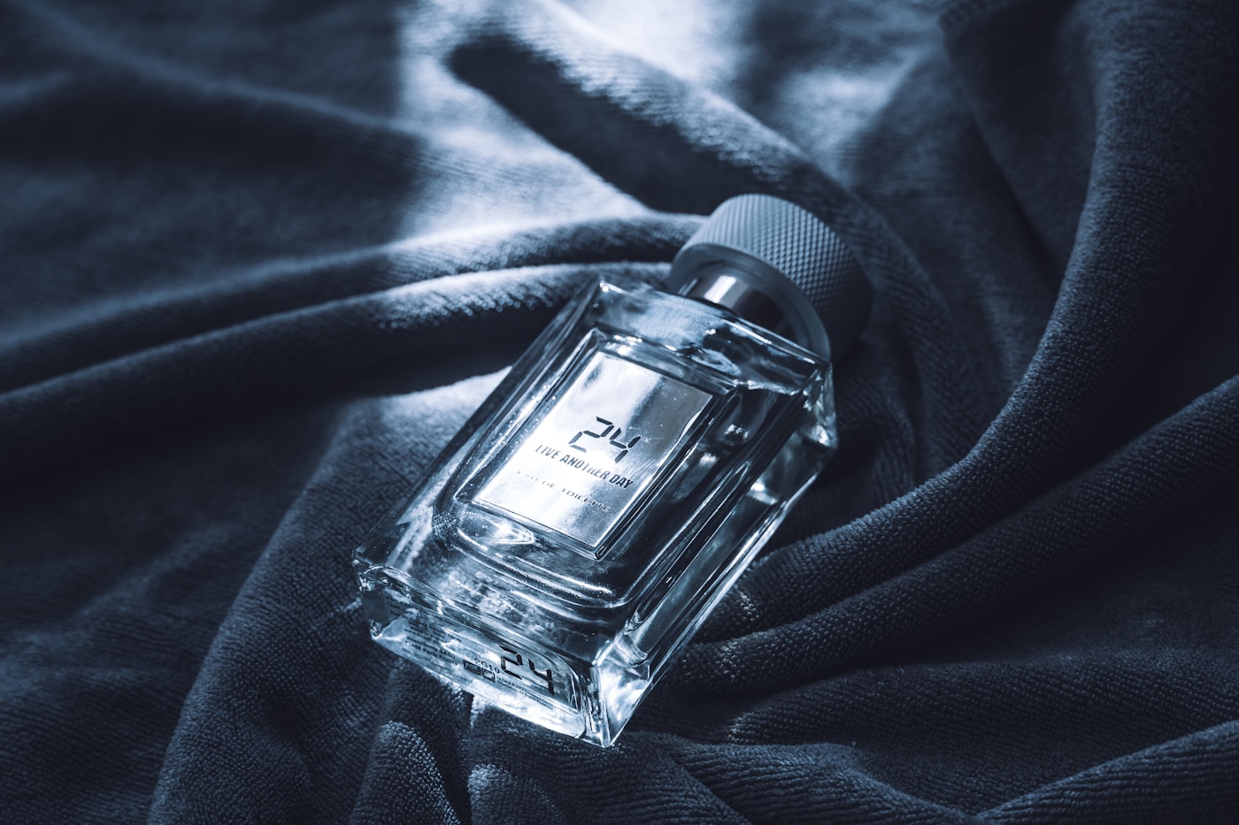 Clear perfume bottle lit in cool blue on dark folded fabric