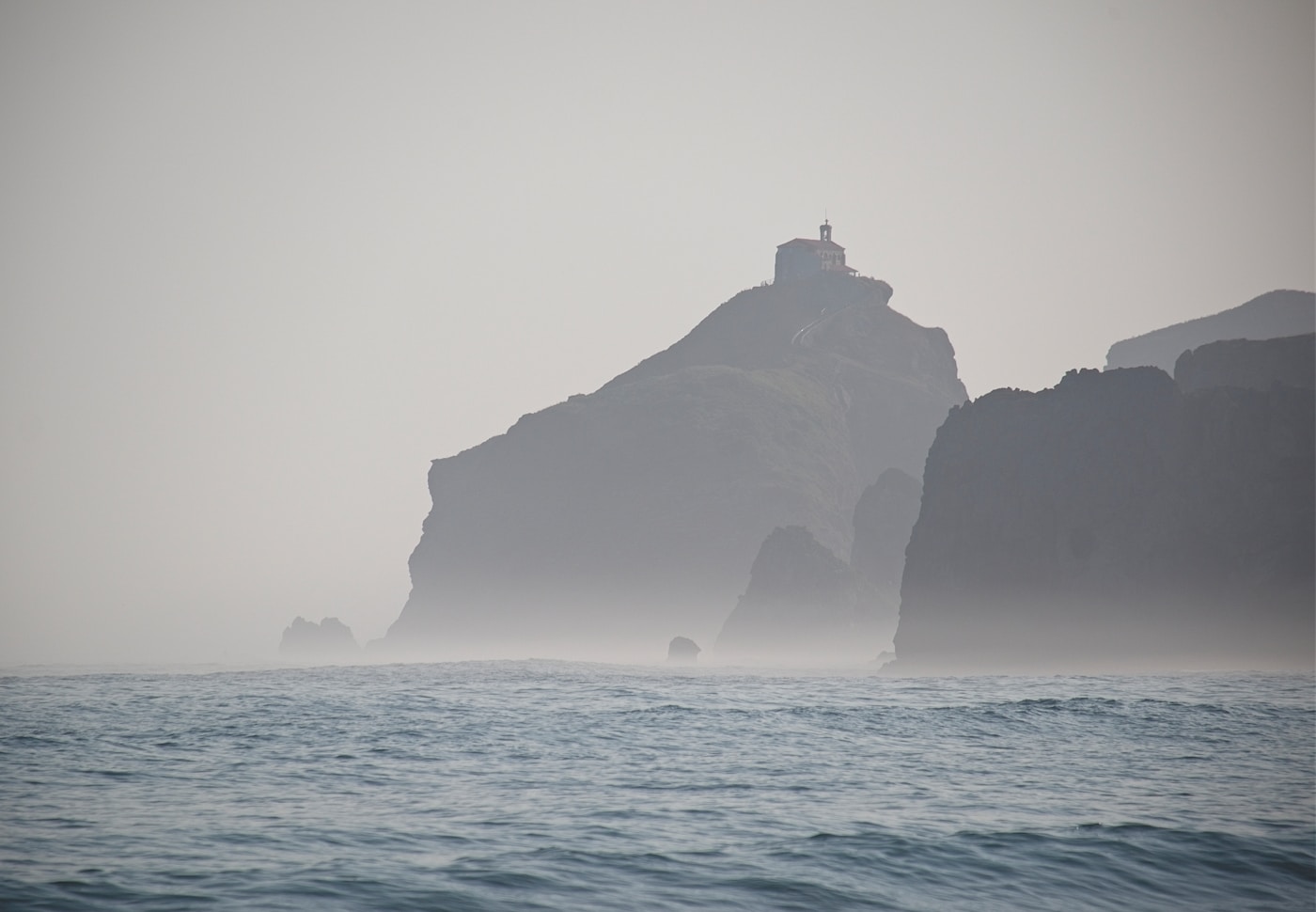 Misty coastal cliffs with a small lighthouse in the distance